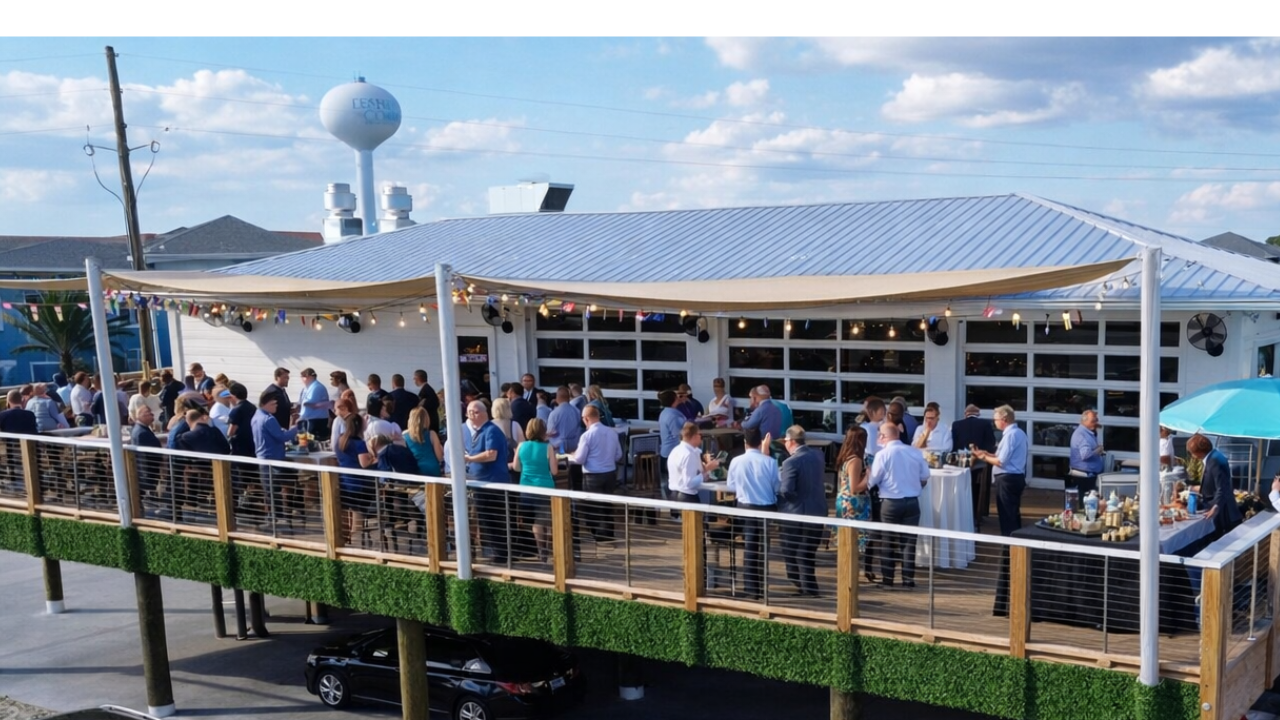 A large group mingles on a deck beside a modern white building at an event space in Fort Walton Beach.